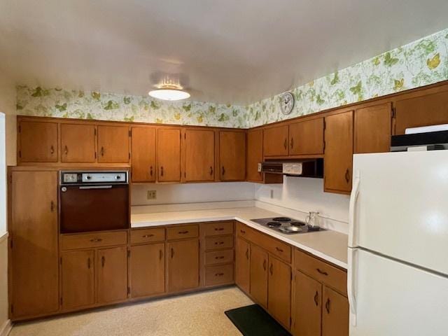 kitchen featuring freestanding refrigerator, wall oven, stainless steel electric stovetop, wallpapered walls, and under cabinet range hood