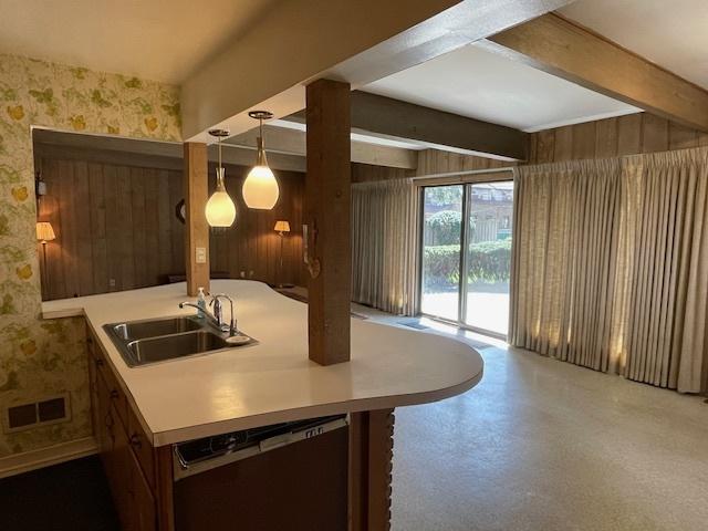 kitchen with a sink, dishwasher, wallpapered walls, beamed ceiling, and visible vents