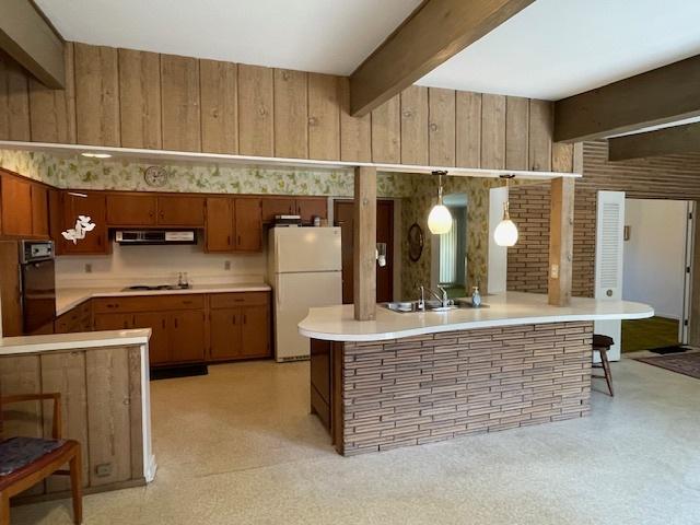 kitchen with brown cabinets, beam ceiling, light countertops, cooktop, and freestanding refrigerator