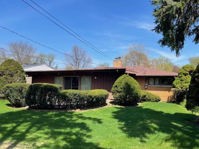 view of front of house featuring board and batten siding, a chimney, and a front lawn