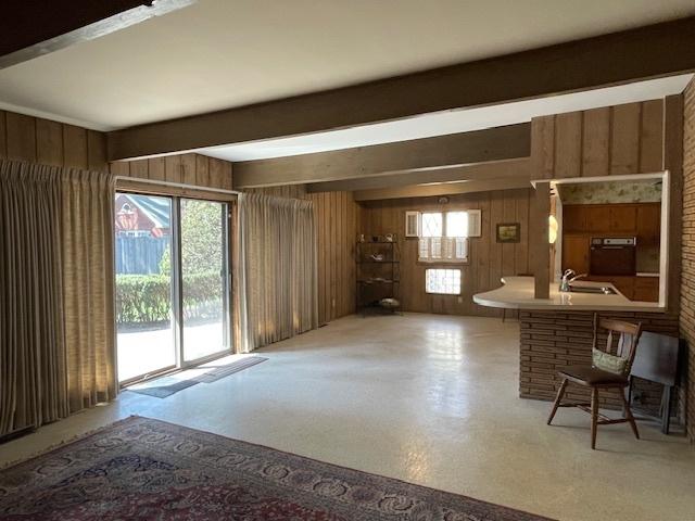 unfurnished living room featuring beamed ceiling, wood walls, and a sink
