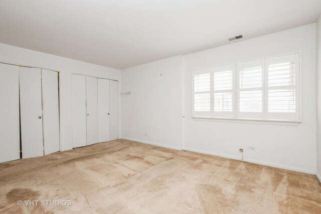 unfurnished bedroom featuring visible vents, multiple closets, carpet floors, and baseboards