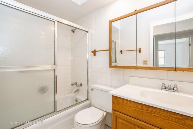bathroom with tile walls, vanity, toilet, and shower / bath combination with glass door