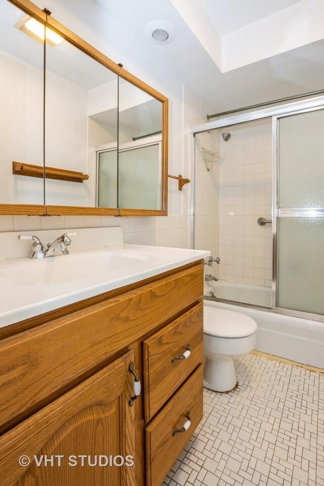 bathroom with toilet, tile walls, combined bath / shower with glass door, and vanity