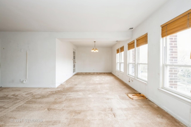 spare room featuring light colored carpet and a notable chandelier