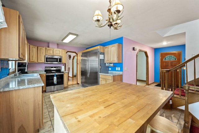 kitchen with an inviting chandelier, light tile patterned flooring, light countertops, arched walkways, and appliances with stainless steel finishes