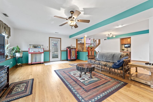 living room featuring light wood finished floors, a ceiling fan, baseboards, visible vents, and stairway