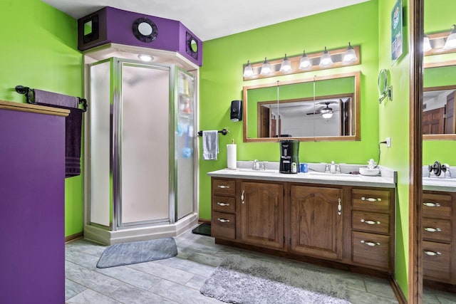 full bathroom with double vanity, a ceiling fan, a shower stall, and a sink