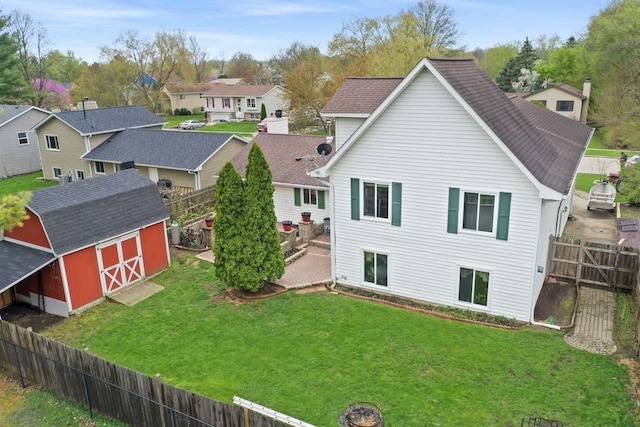 back of house featuring a residential view, a shed, a fenced backyard, a lawn, and an outdoor structure