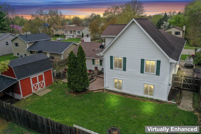 rear view of house featuring a residential view, a shed, a fenced backyard, an outbuilding, and a lawn