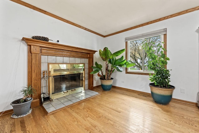 unfurnished living room with visible vents, a tiled fireplace, crown molding, wood finished floors, and baseboards