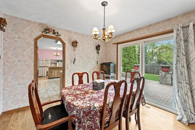 dining area with arched walkways, baseboards, light wood finished floors, a notable chandelier, and wallpapered walls
