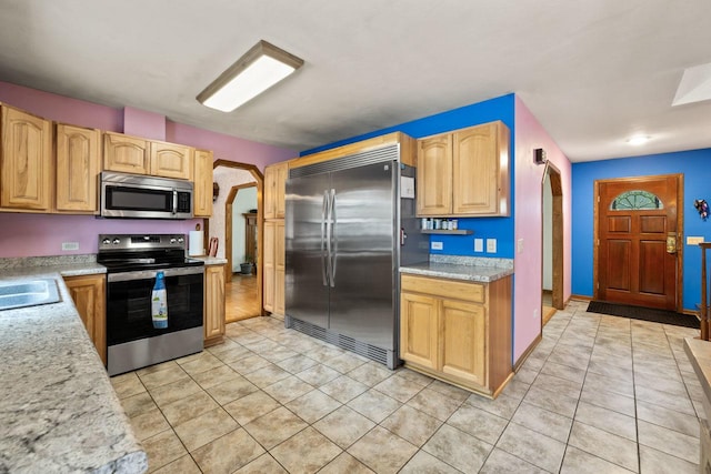 kitchen with stainless steel appliances, arched walkways, a sink, and light tile patterned floors