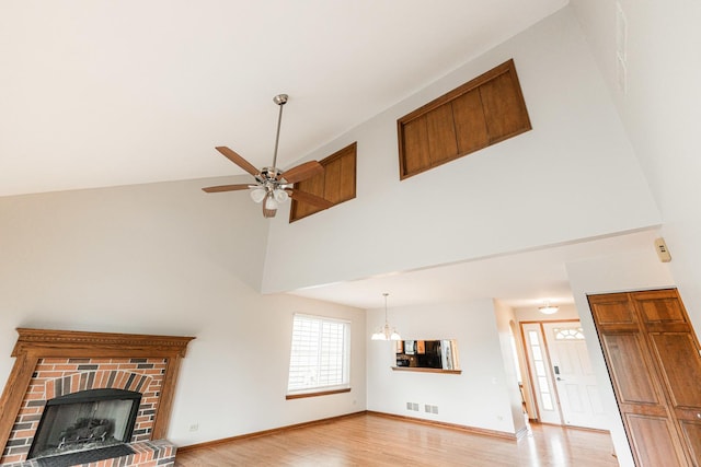 unfurnished living room with a fireplace, light wood-style floors, a ceiling fan, baseboards, and a towering ceiling