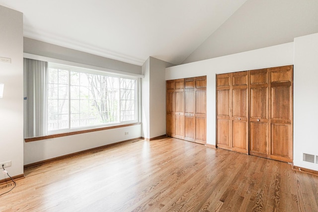 unfurnished bedroom featuring light wood-style floors, multiple closets, baseboards, lofted ceiling, and visible vents