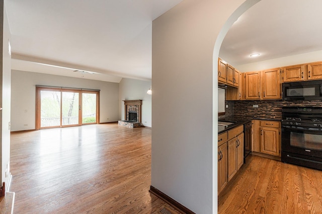kitchen featuring dark countertops, open floor plan, decorative backsplash, wood finished floors, and black appliances