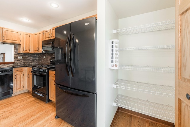 kitchen with dark countertops, light brown cabinets, light wood-style floors, decorative backsplash, and black appliances