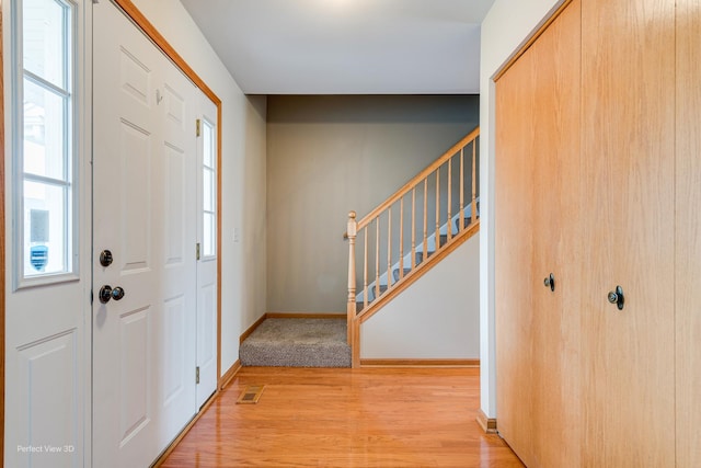 foyer entrance with stairway, baseboards, and light wood-type flooring