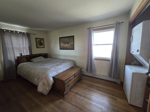 bedroom with wood-type flooring, stacked washer and clothes dryer, and a baseboard radiator