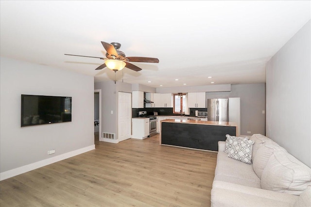 living area featuring a ceiling fan, light wood-style flooring, baseboards, visible vents, and recessed lighting