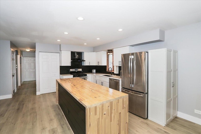 kitchen with a center island, light wood-style flooring, a sink, wall chimney range hood, and appliances with stainless steel finishes