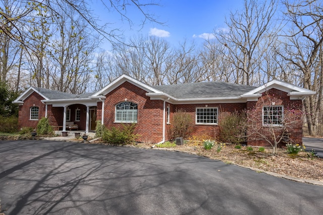 single story home featuring a porch, brick siding, and a shingled roof