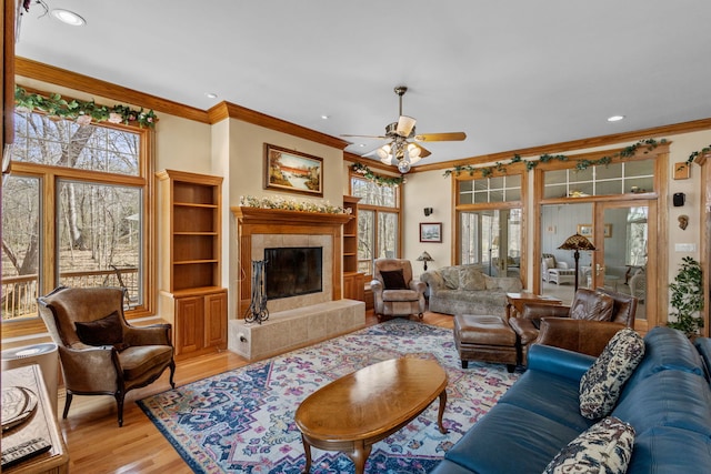 living area with light wood-style floors, ceiling fan, crown molding, healthy amount of natural light, and a high end fireplace