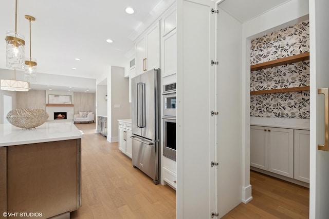 87 Windmill Rd, Orland Park, IL 60467 - kitchen featuring appliances with stainless steel finishes, light wood finished floors, open floor plan, light countertops, and a warm lit fireplace