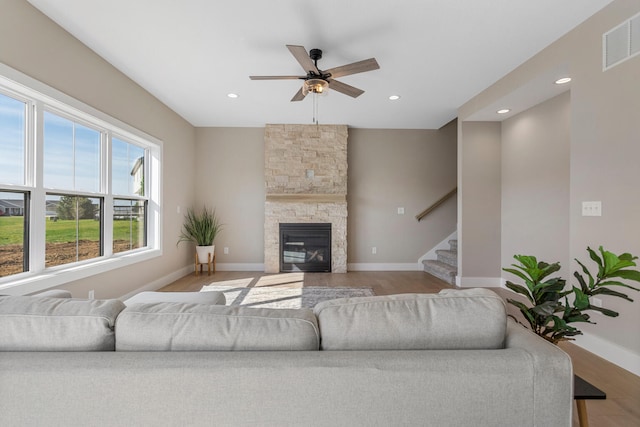 living area featuring ceiling fan, baseboards, wood finished floors, visible vents, and stairway