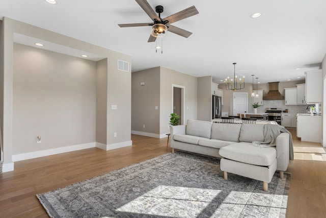living room featuring baseboards, visible vents, light wood-style flooring, and ceiling fan with notable chandelier