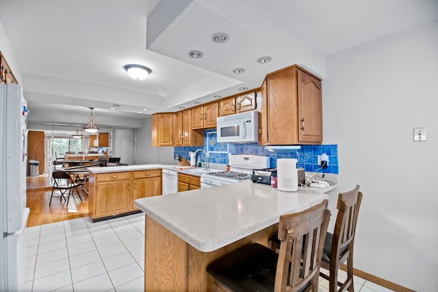kitchen featuring a peninsula, backsplash, white appliances, light countertops, and light tile patterned floors