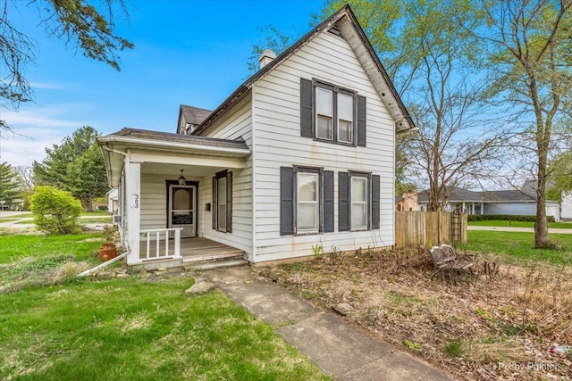 view of front of home featuring covered porch, fence, a chimney, and a front yard
