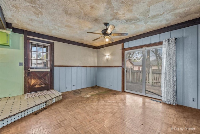 empty room with a wainscoted wall, visible vents, and ceiling fan