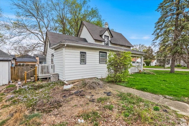 rear view of house with a lawn, fence, and roof with shingles