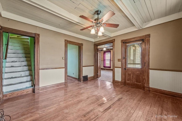 empty room with beamed ceiling, light wood-type flooring, a ceiling fan, wood ceiling, and wainscoting
