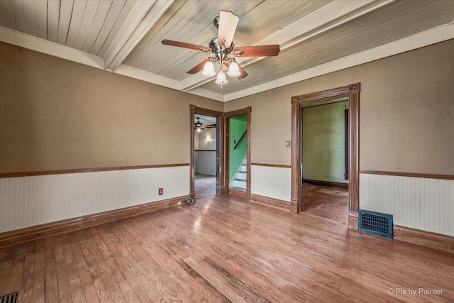 empty room featuring wood ceiling, beamed ceiling, ceiling fan, hardwood / wood-style floors, and stairs