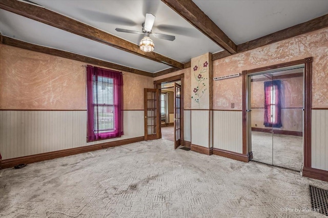 spare room with visible vents, a wainscoted wall, carpet floors, beam ceiling, and a ceiling fan