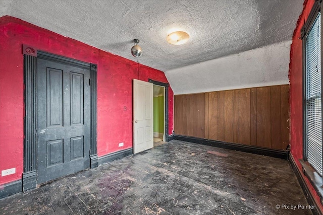 additional living space with baseboards, wooden walls, a textured ceiling, and vaulted ceiling