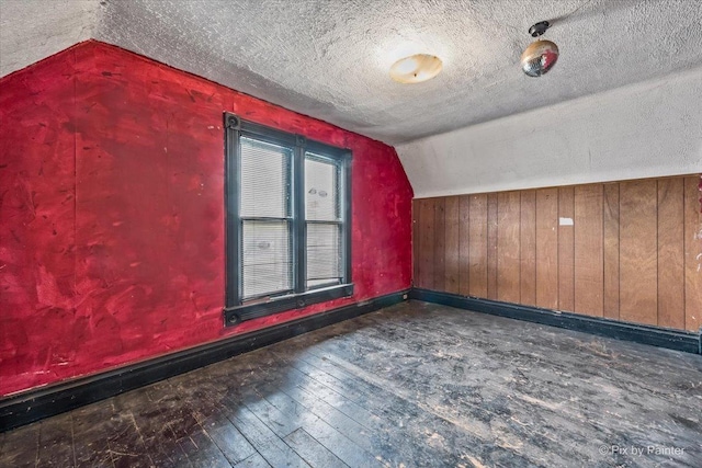 additional living space with lofted ceiling, a textured ceiling, wood walls, baseboards, and wood-type flooring