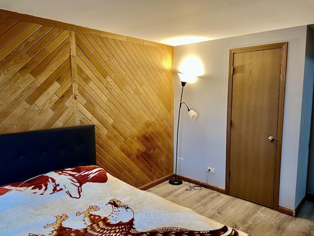 bedroom featuring baseboards, wooden walls, and light wood-type flooring