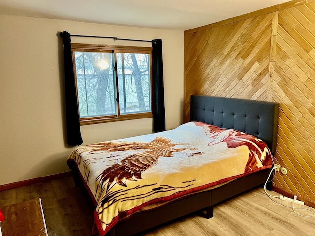 bedroom with baseboards, wood finished floors, and wooden walls