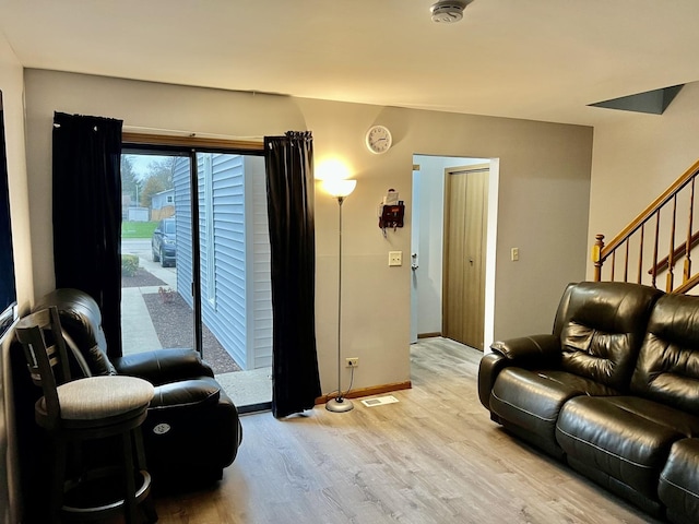 living room featuring baseboards, stairs, visible vents, and light wood-style flooring