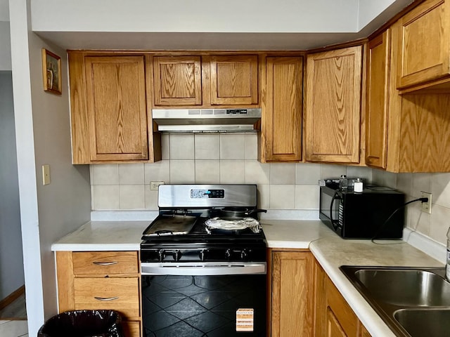 kitchen with a sink, brown cabinetry, under cabinet range hood, black microwave, and stainless steel range with gas stovetop