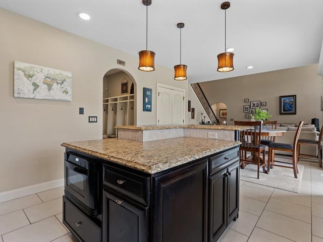 kitchen with dark cabinetry, arched walkways, pendant lighting, and light tile patterned floors