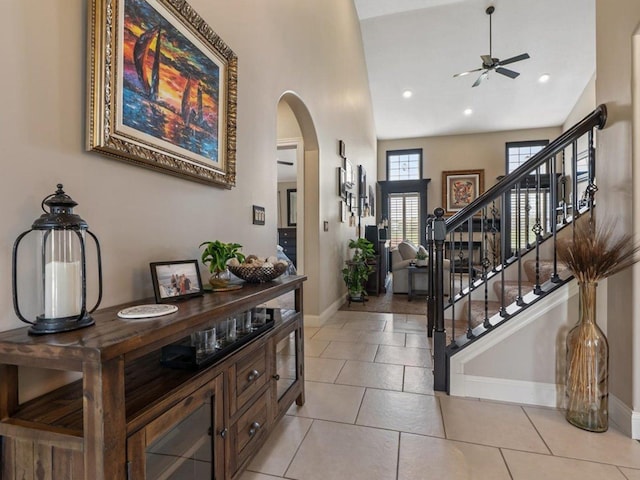 foyer with a ceiling fan, stairs, baseboards, arched walkways, and light tile patterned floors
