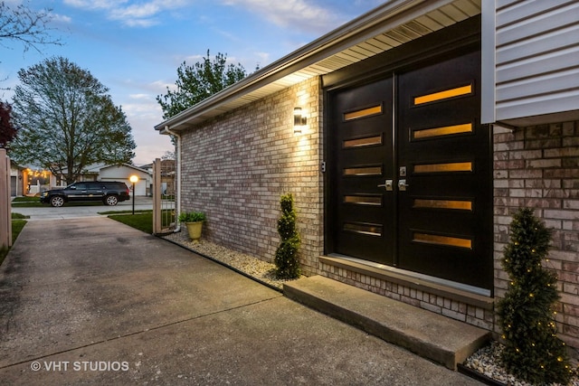 entrance to property featuring brick siding, a garage, french doors, and concrete driveway