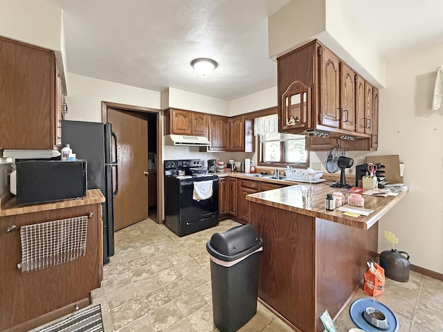 kitchen with brown cabinetry, black appliances, light countertops, a peninsula, and range hood