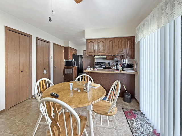 kitchen with exhaust hood, light countertops, black appliances, a peninsula, and brown cabinetry