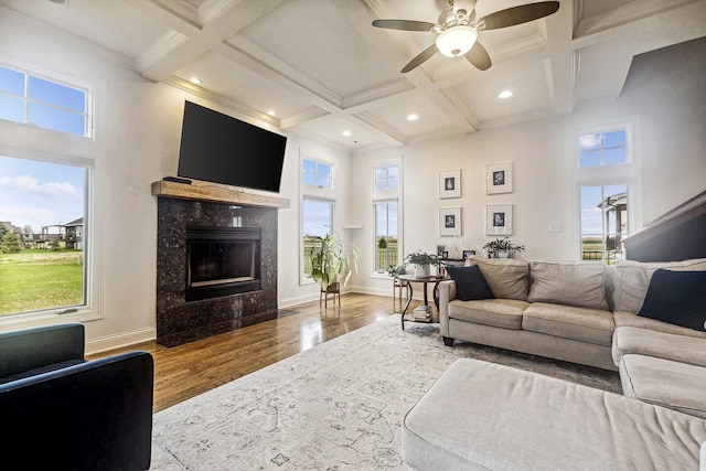 living area with coffered ceiling, a ceiling fan, wood finished floors, a high ceiling, and a fireplace