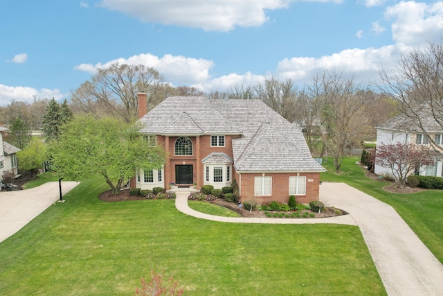 view of front of home featuring driveway, a chimney, a front yard, and brick siding